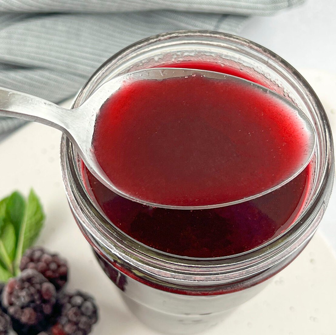 Blackberry simple syrup on a spoon with frozen blackberries on the left.