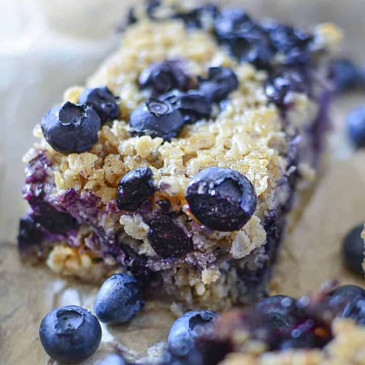 One blueberry oat square with fresh blueberries around it.