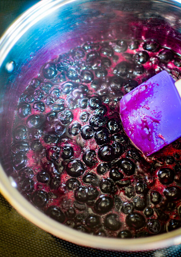 Blueberries in a pot that are cooking down and making their own juice.