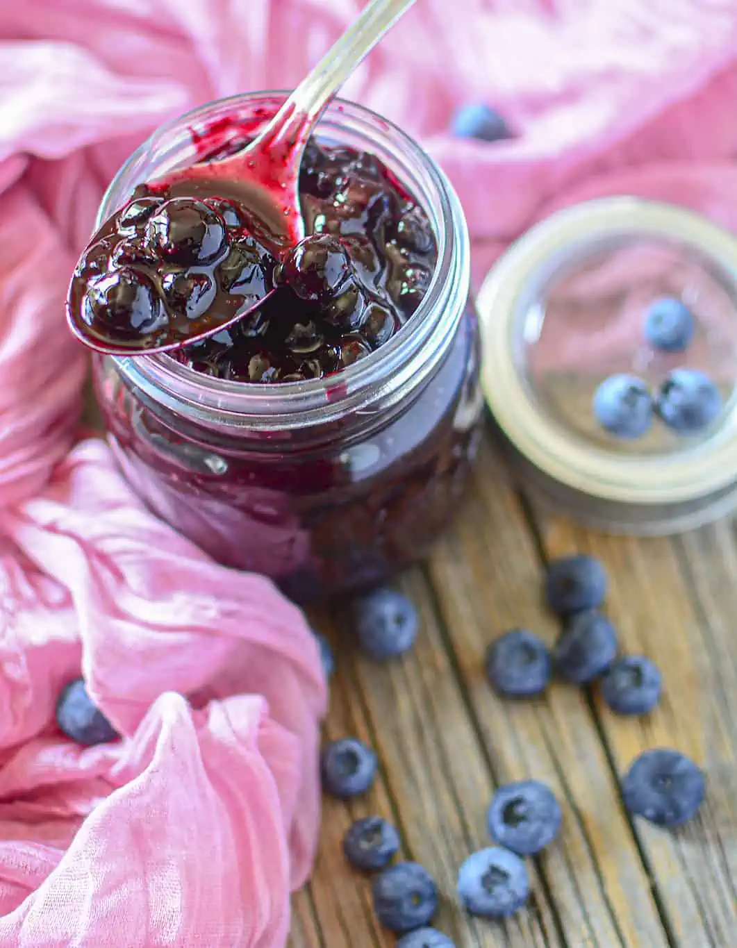 Blueberry pie filling in a glass jar with a spoon on top.