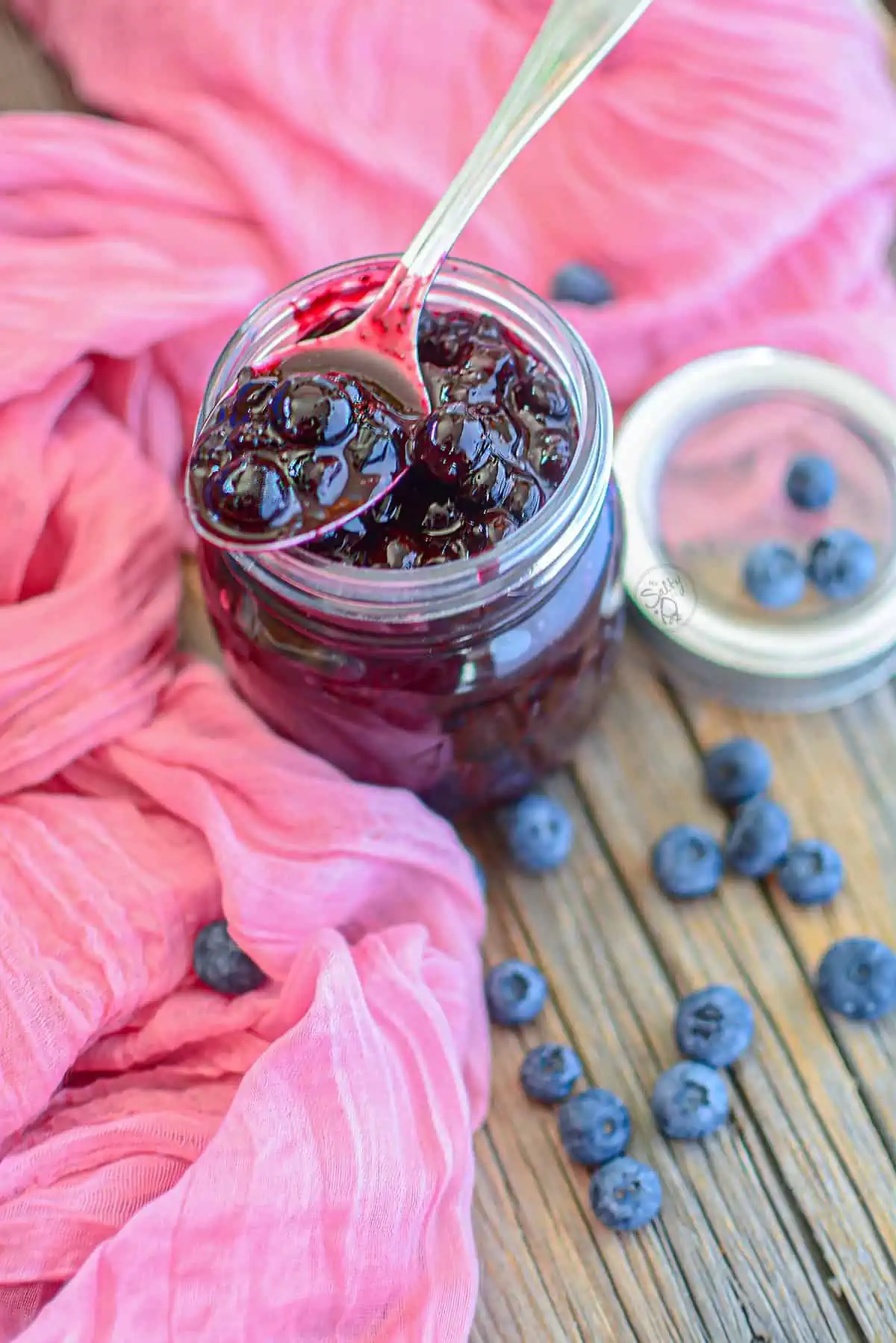 Berry pie filling with a spoon resting on the top of the jar on a wooden background.