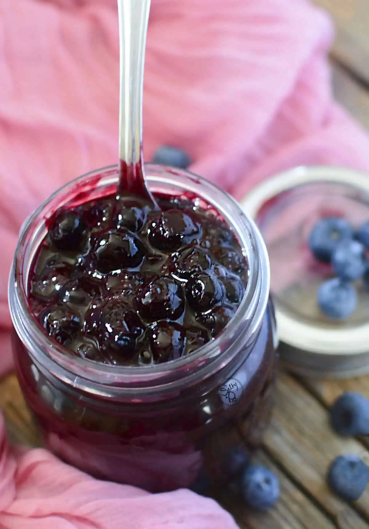 Berry pie filling on a wooden background with a spoon sticking out of the top of the jar.