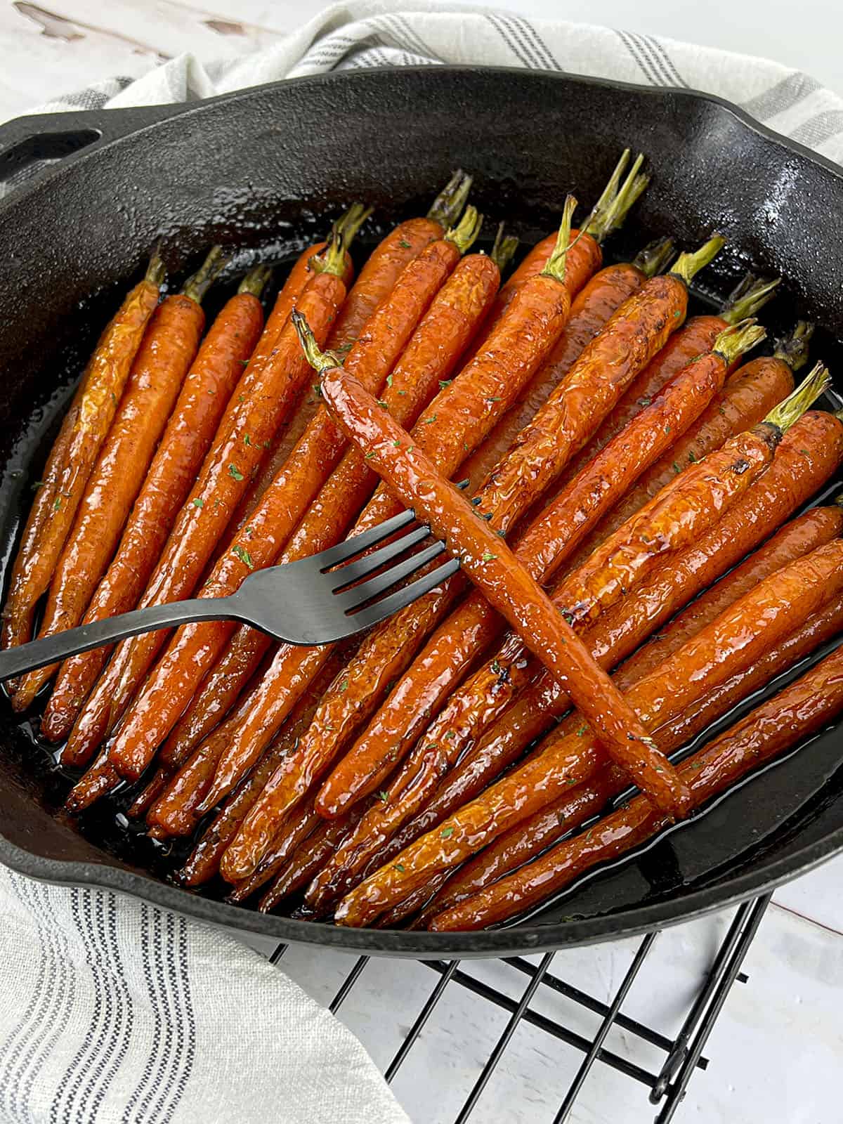 The roasted carrots are in a pan with a fork peircing one of the cooked carrots.
