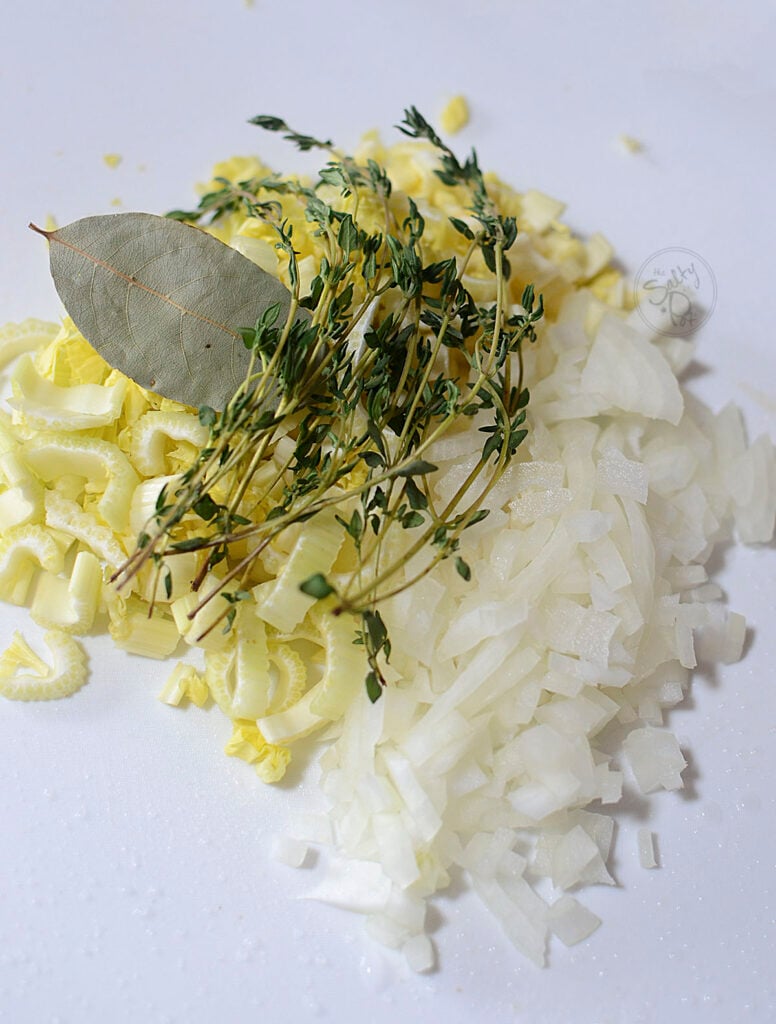 Onions, celery, bay leaves and fresh time on a white cutting board.