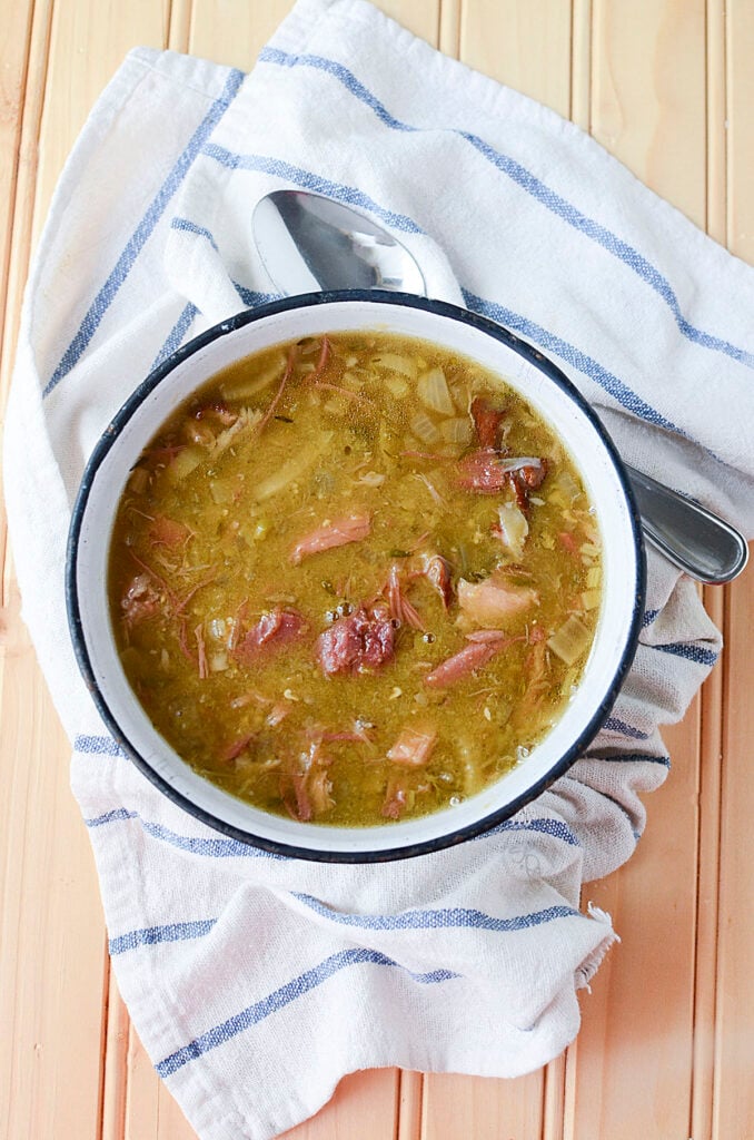 Smoked pork hock soup in a white bowl, with a blue and white napkin underneath. A spoon is on the upper right side.