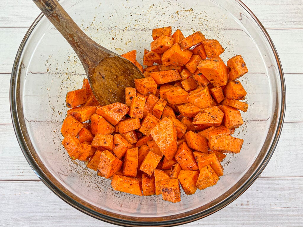 Seasoned raw sweet potatoes in a bowl.