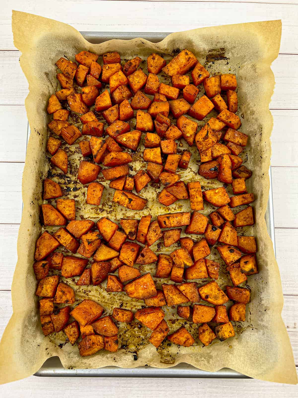 Roasted sweet potato cubes on a sheet pan with parchment paper.