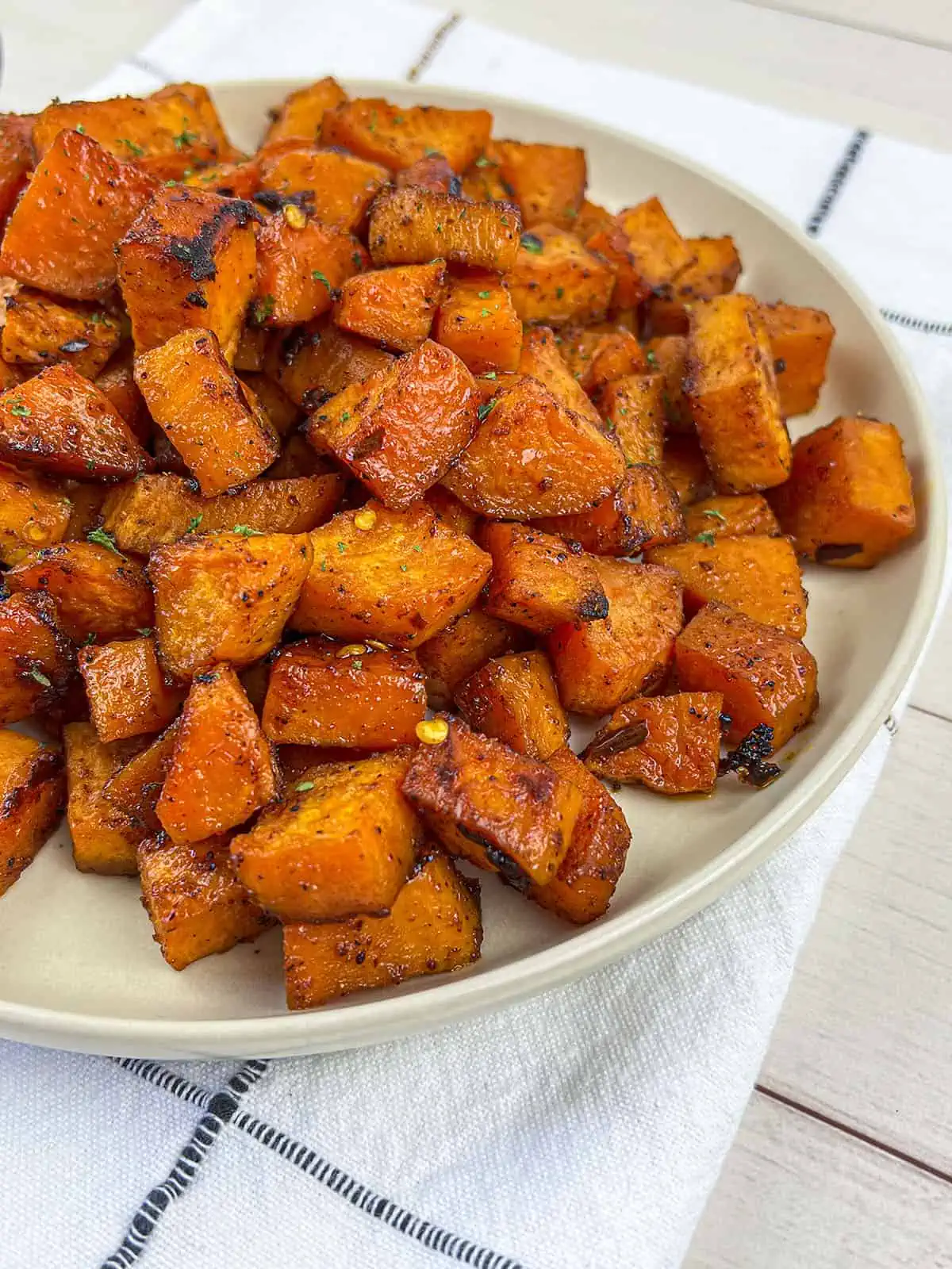 Sweet potato cubes that have been cooked on a plate with a white and blue striped napkin underneath.