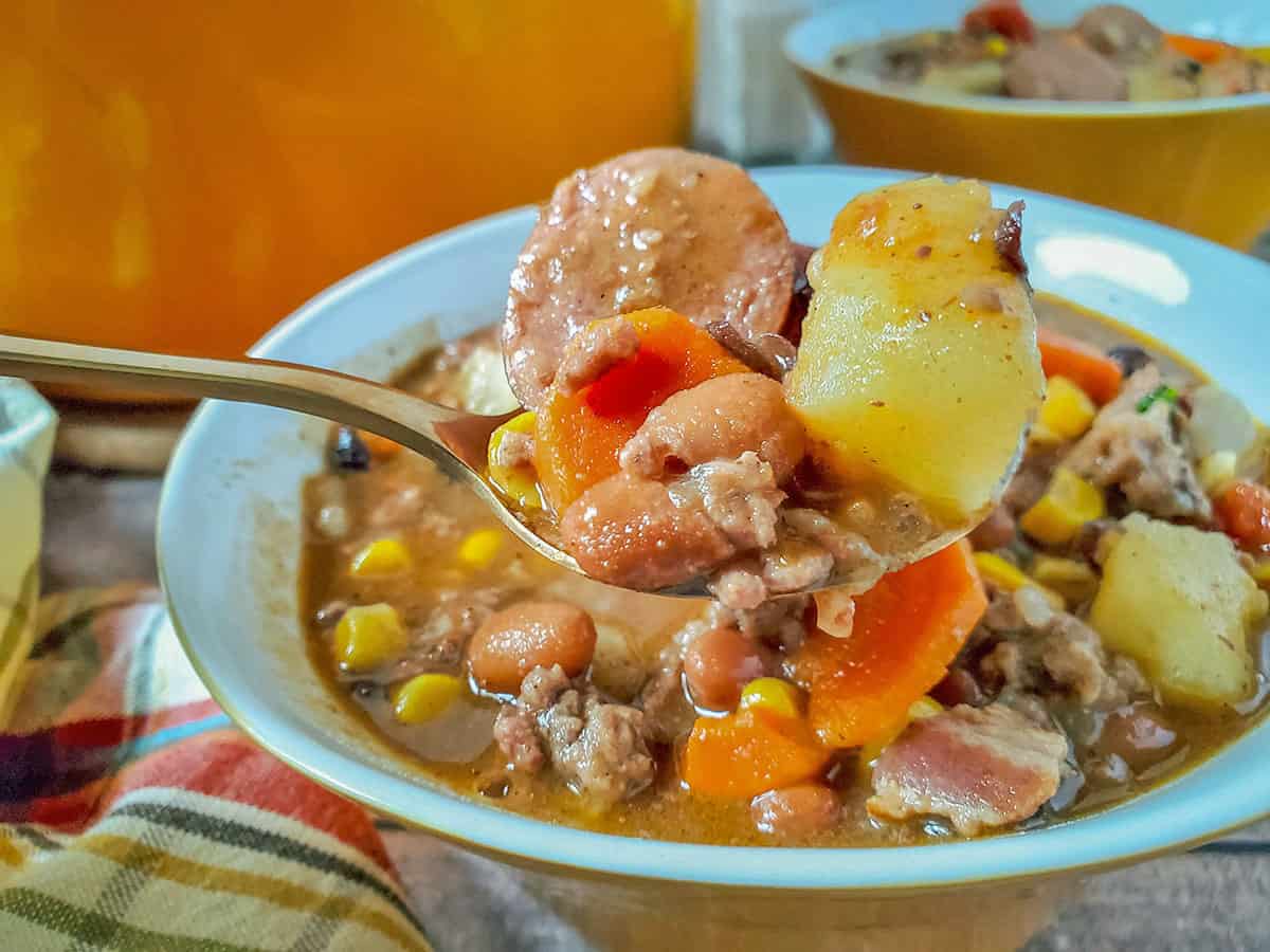 A spoonful of the cowboy soup with the blue bowl in the background.