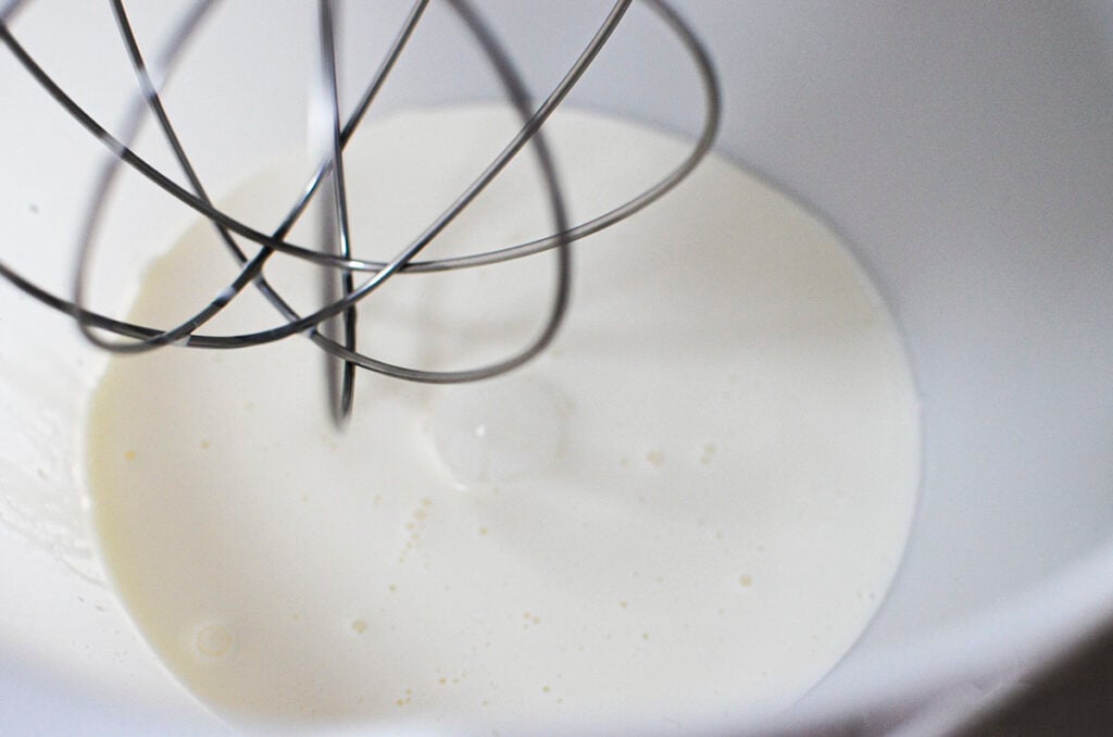 Whipping cream in a bowl with a whisk attachment, ready to make butter.