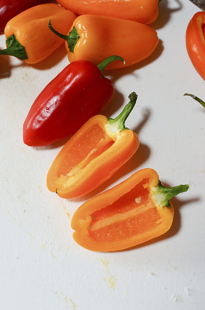 Sliced mini bell peppers on a white cutting board.