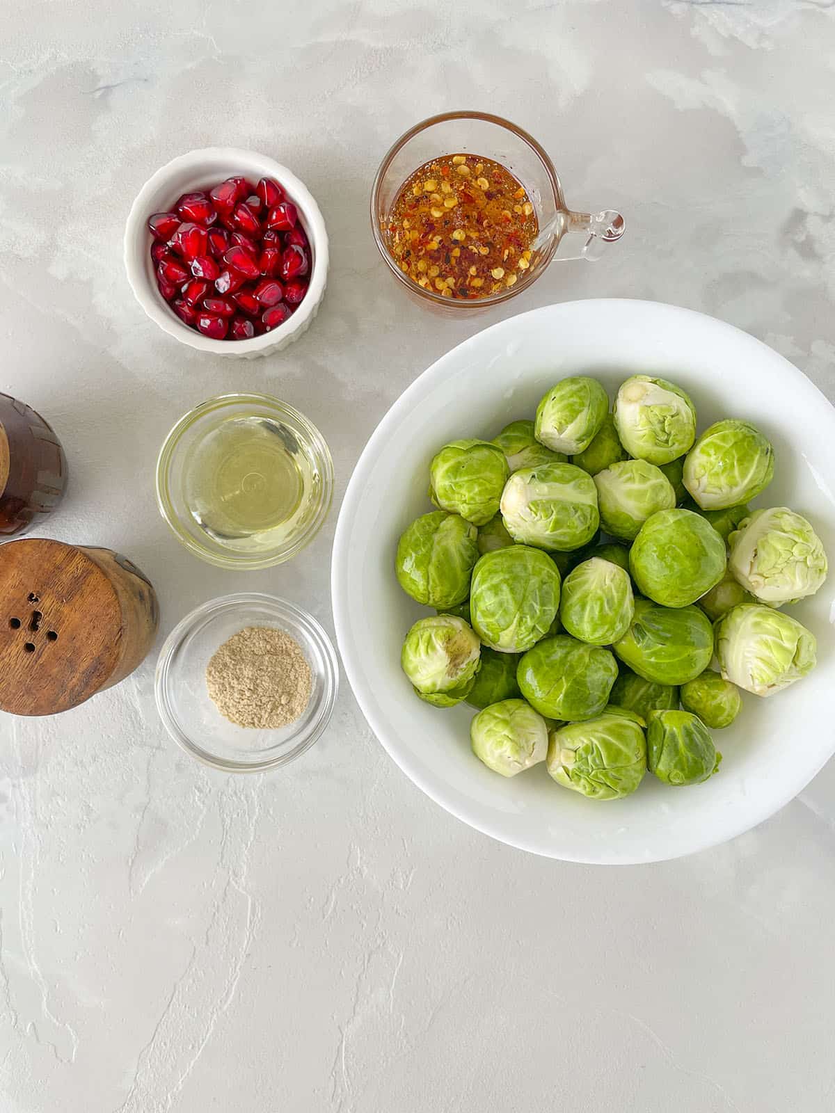 Ingredients for this dish such as brussels sprouts, garlic powder, hot honey, pomegranate ariels, oil and salt and pepper.