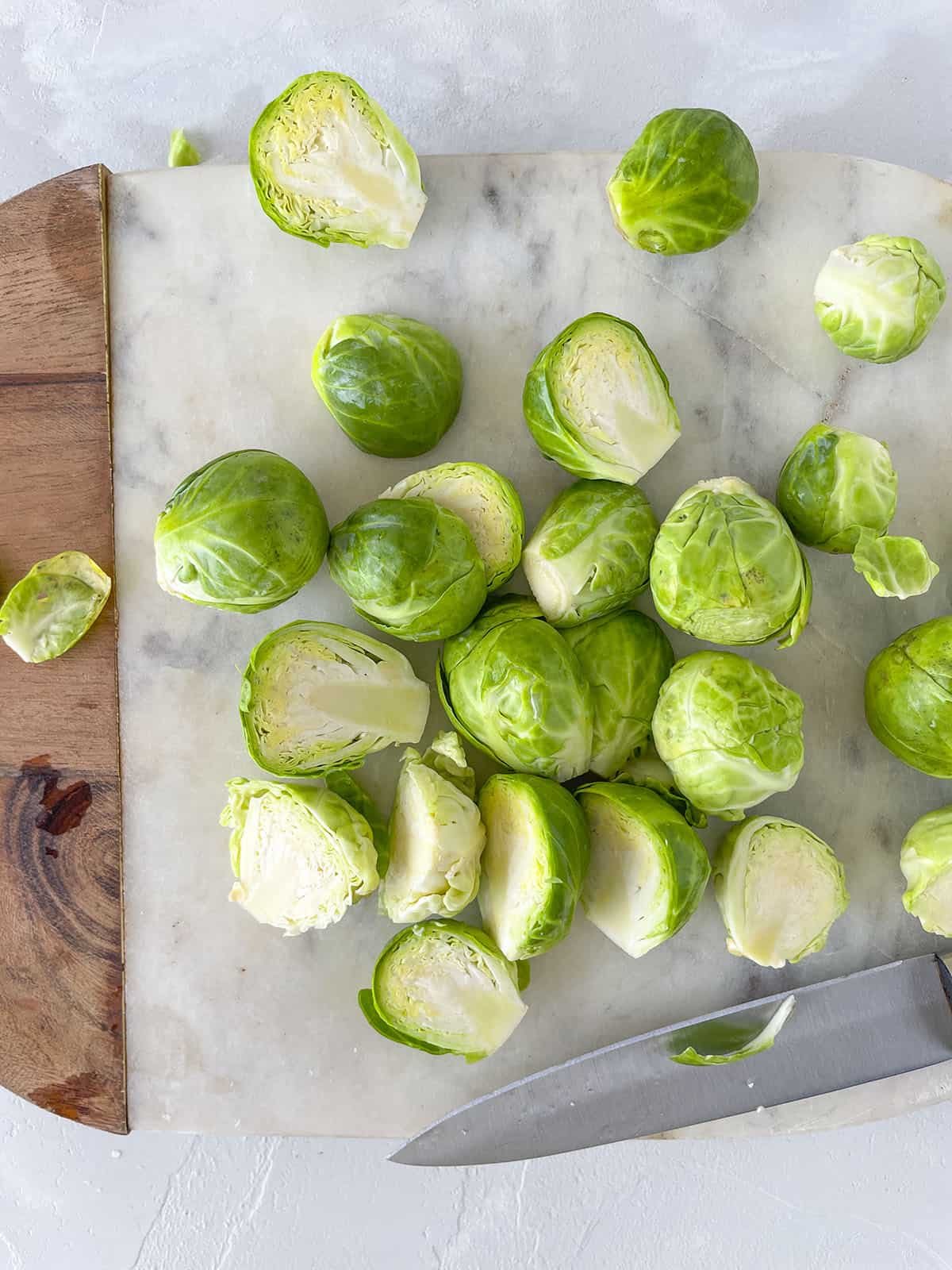 Brussels sprouts sliced in half, sitting on a marble cutting board. 