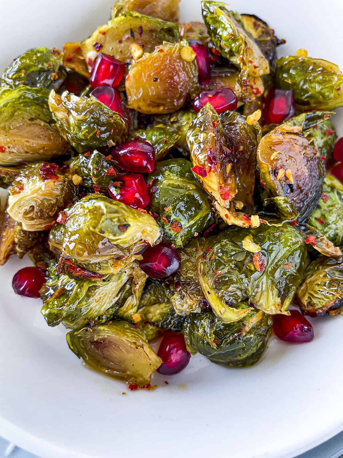 Roasted sprouts with hot honey and pomegranate ariels in a white bowl. 