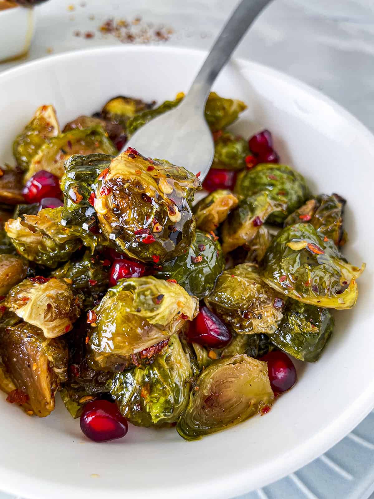 A fork holding a roasted brussels sprout with hot honey. 