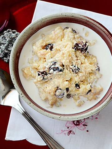 nstant Pot Eggnog rice pudding with cranberries in a red and cream pottery bowl with a cream colored napkin underneath. Square image.