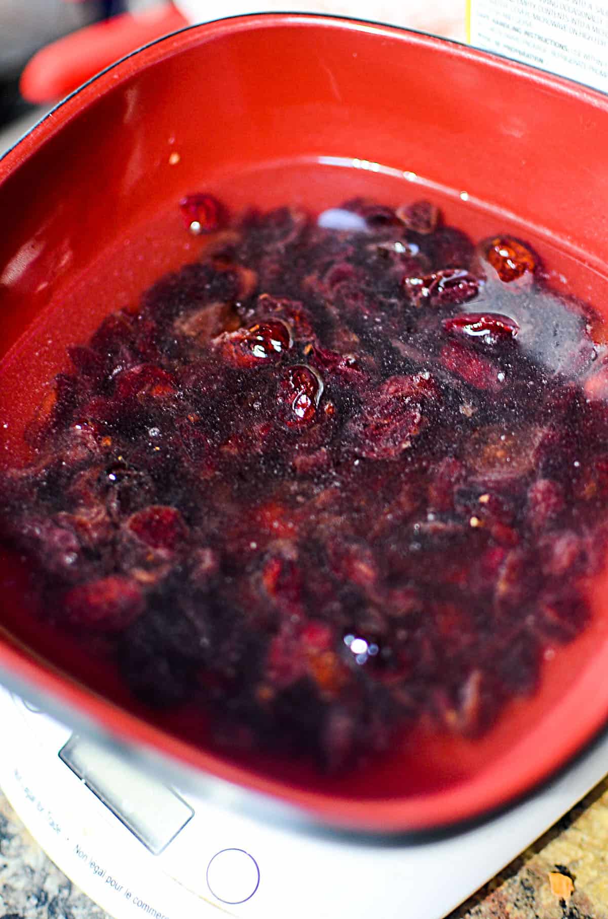 Rehydrating dried cranberries in water, in a red bowl.