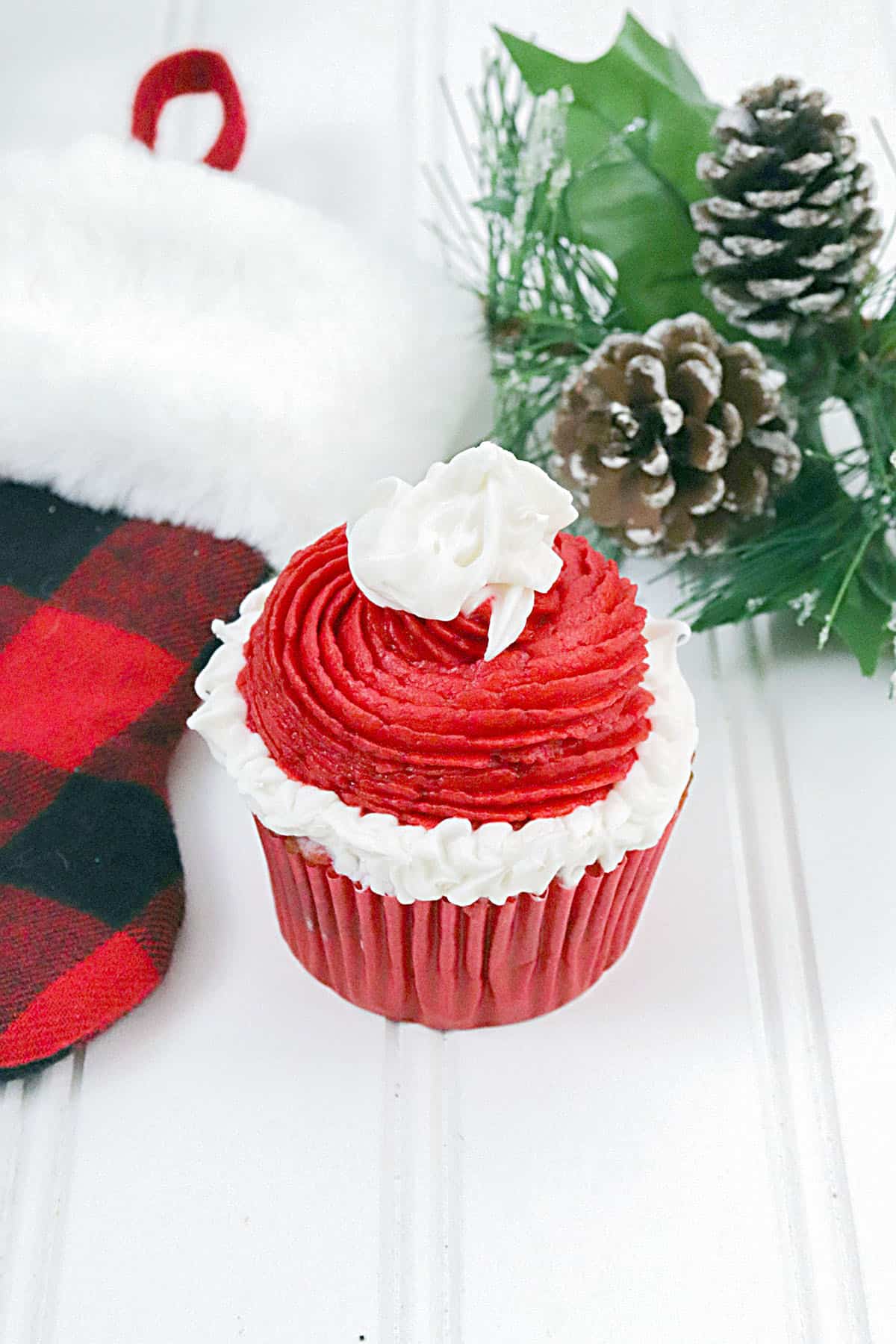 A single red and white cupcake sits in between a plaid stocking and some greenery on the right. 