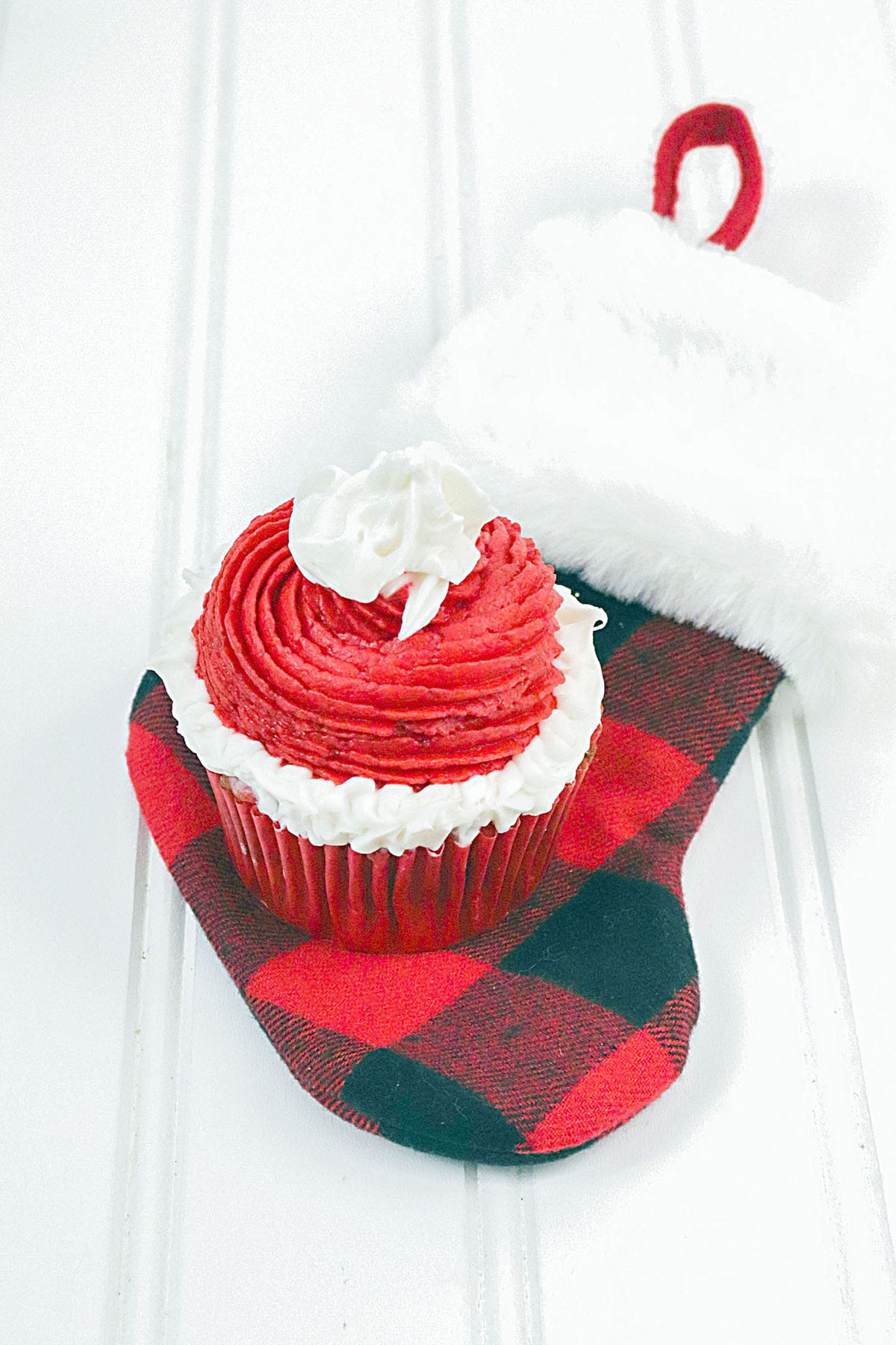 A santa's hat cupcake sitting on a red and white buffalo check stocking.