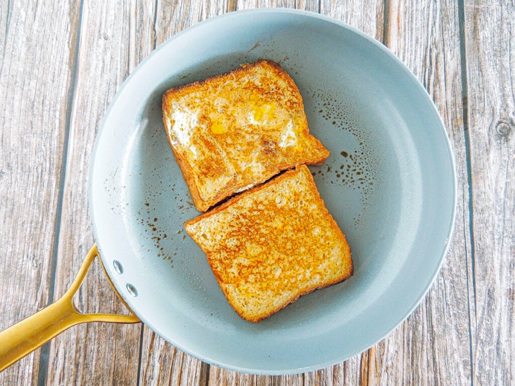 Two slices of french toast cooking in a skillet.