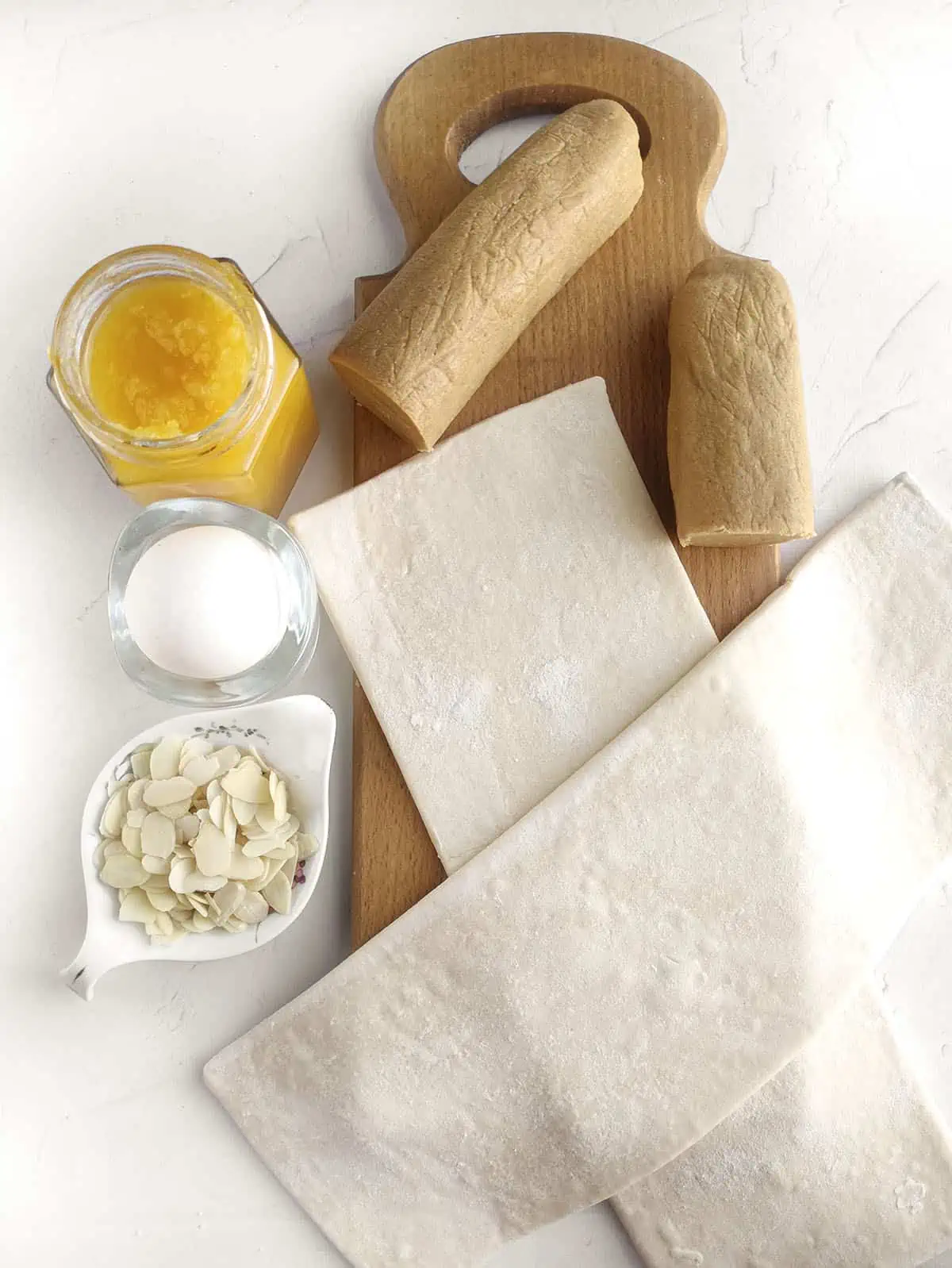 The ingredients to make Dutch Banket. Almond paste, puff pastry, apricot jam, and egg, shaved almonds and icing sugar.