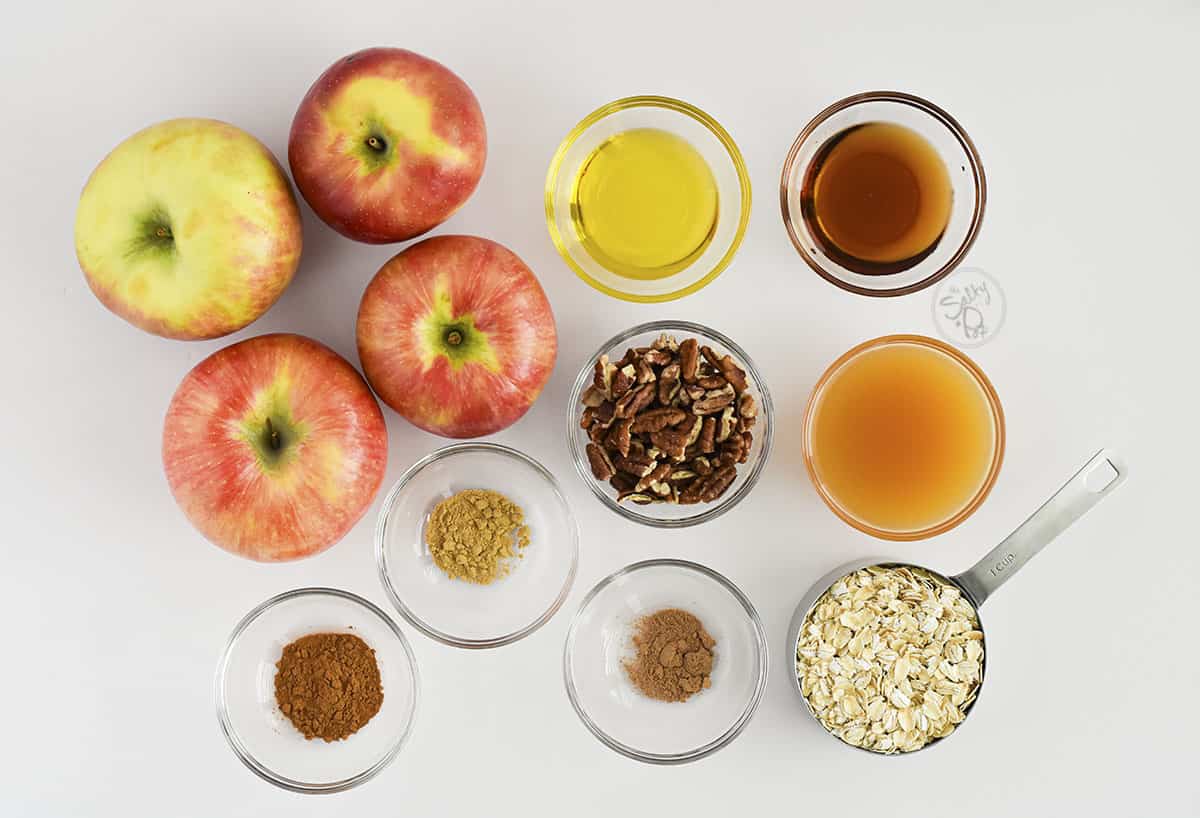 Ingredient photo for this apple recipe. Featured are apples, oil, maple syrup, pecans, apple cider, rolled oats, and spices like ginger, nutmeg and cinnamon.