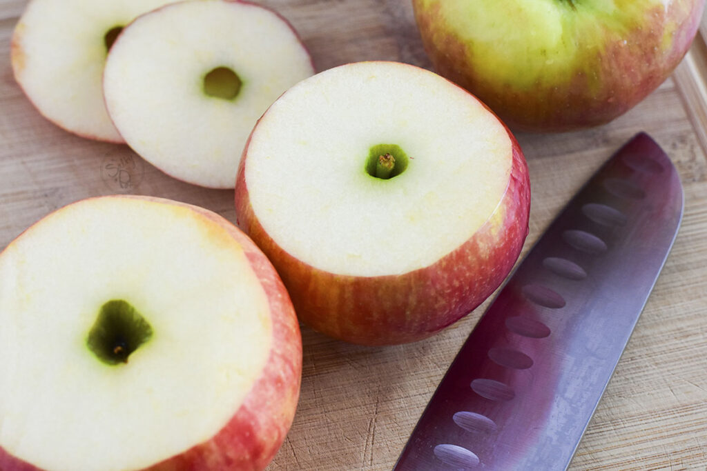 Apples with the tops cut off and a knife on the right of the apples.