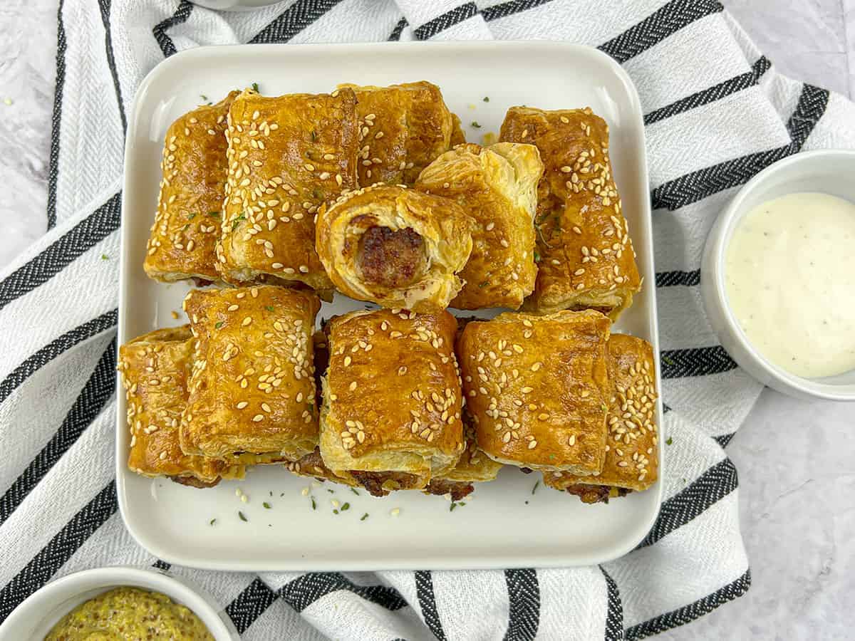 12 air fryer sausage rolls piled on a white square dish with dips on the side.