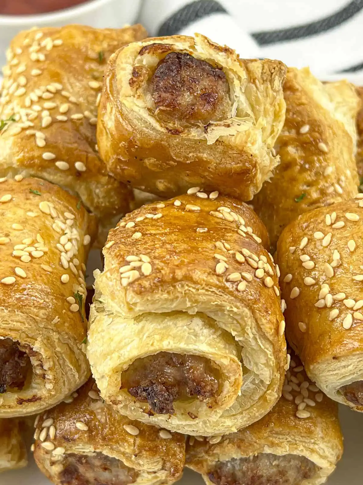 A close up image of the air fryer sausage rolls that show very flaky pastry and the sesame seeds on the top.