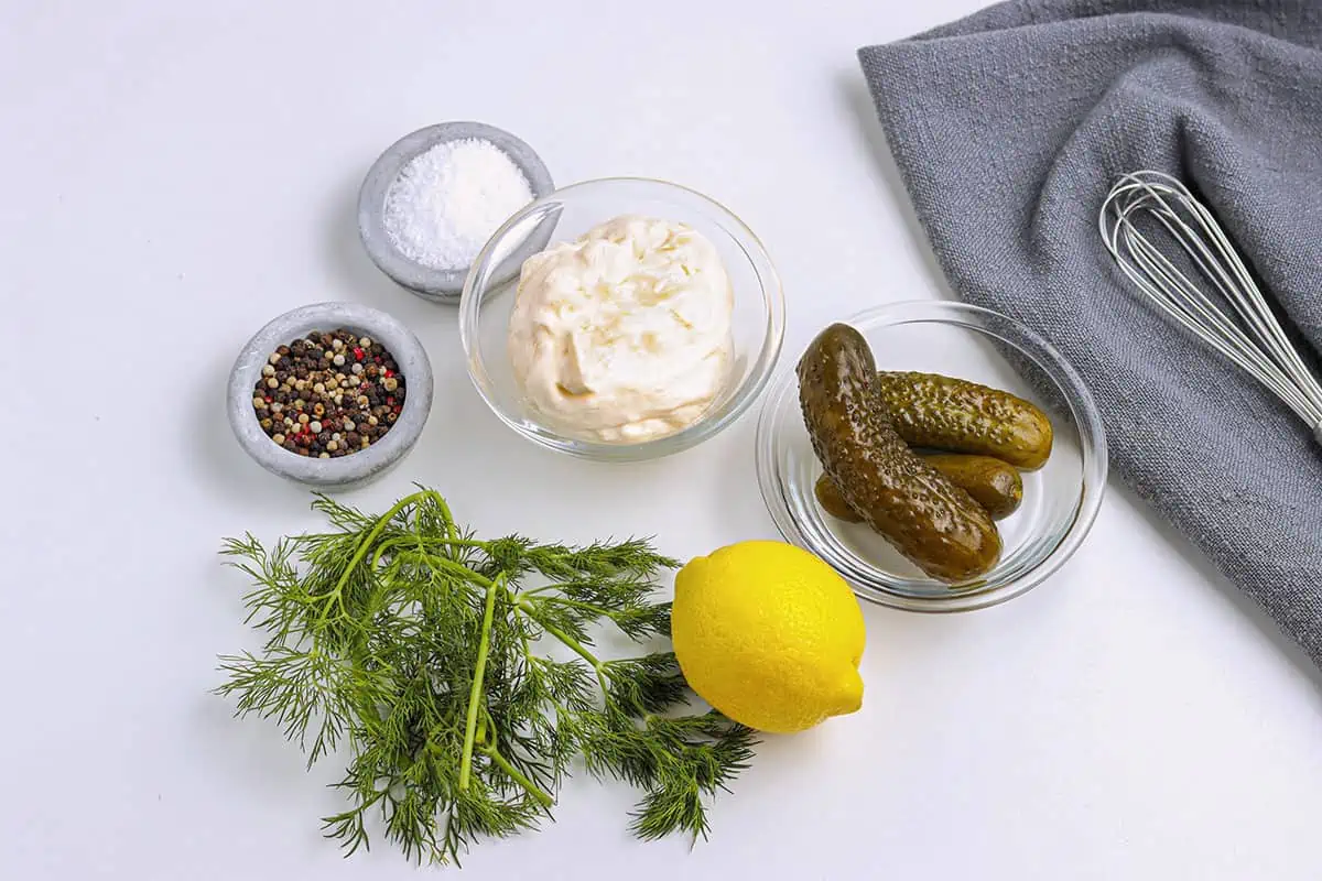 Tartar sauce ingredients on a white table. Fresh dill, pepper, salt, mayonnaise, pickles and fresh lemon.