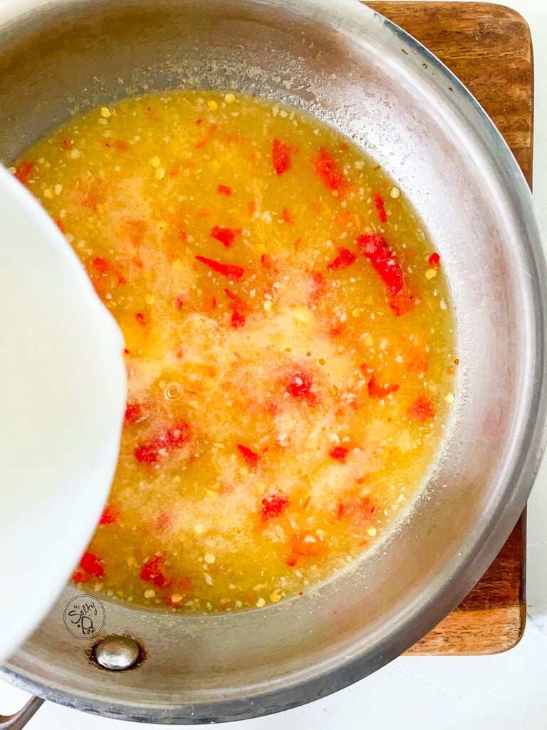 The sweet pineapple chili sauce in a pot, with the cornstarch slurry being added to it. 