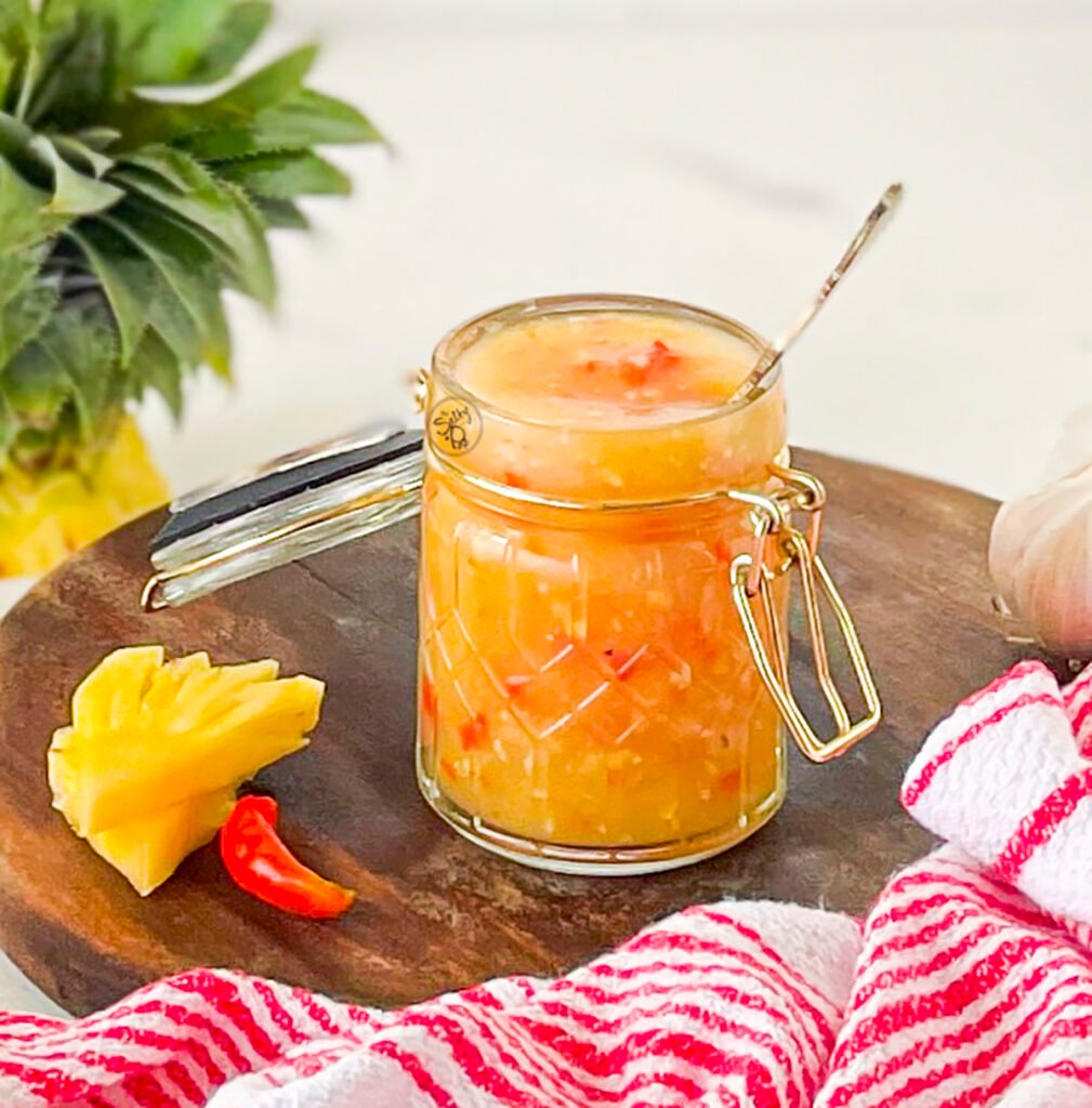 Pineapple chili sauce in a jar on a wooden tray.