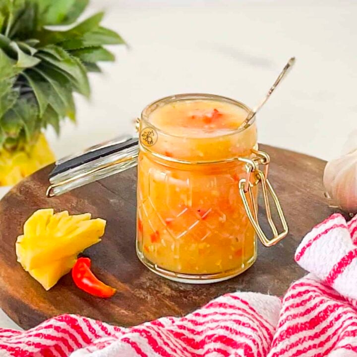 Pineapple chili sauce in a jar on a wooden tray.