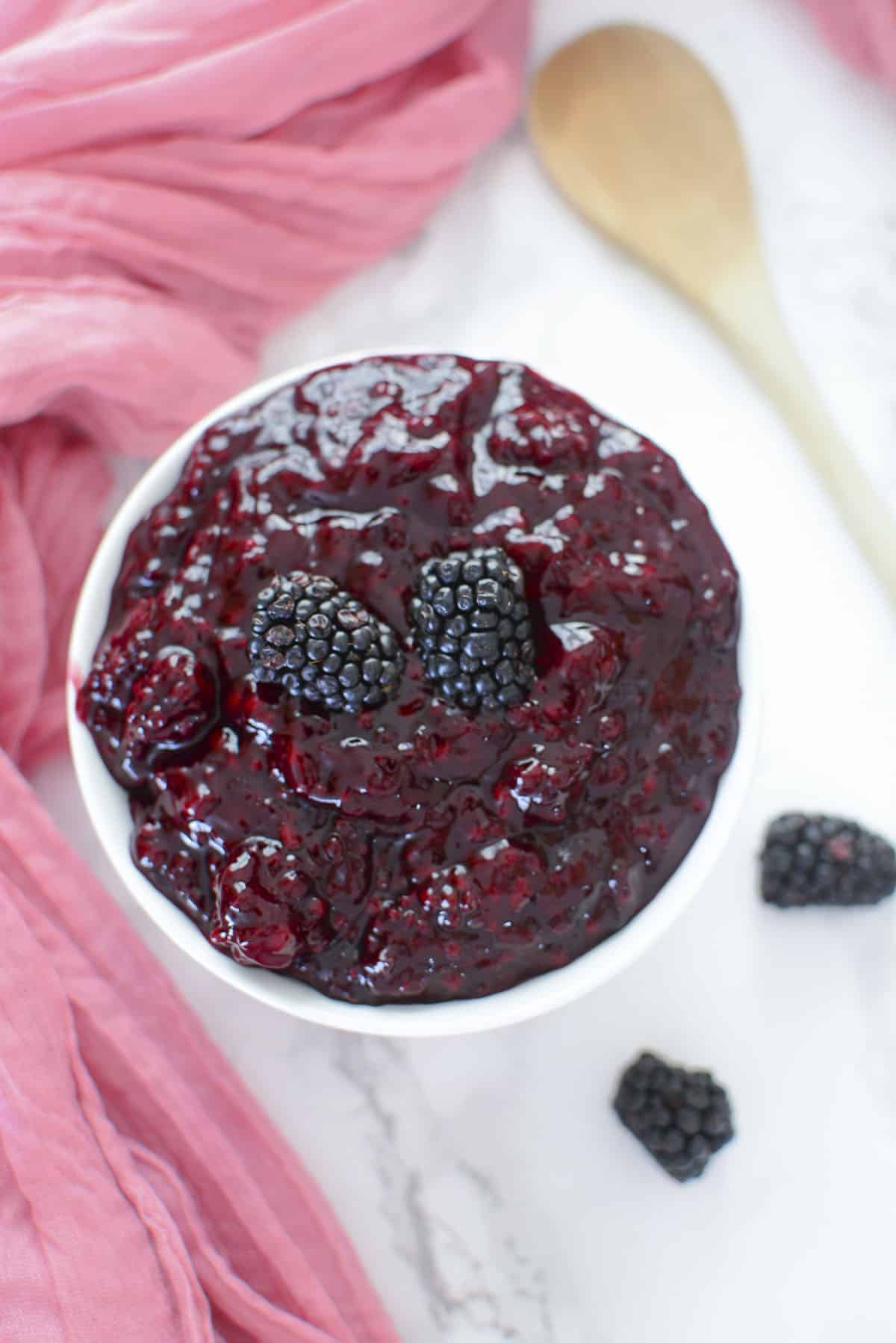 Blackberry pie filling in a white bowl with a wooden spoon on the upper right.