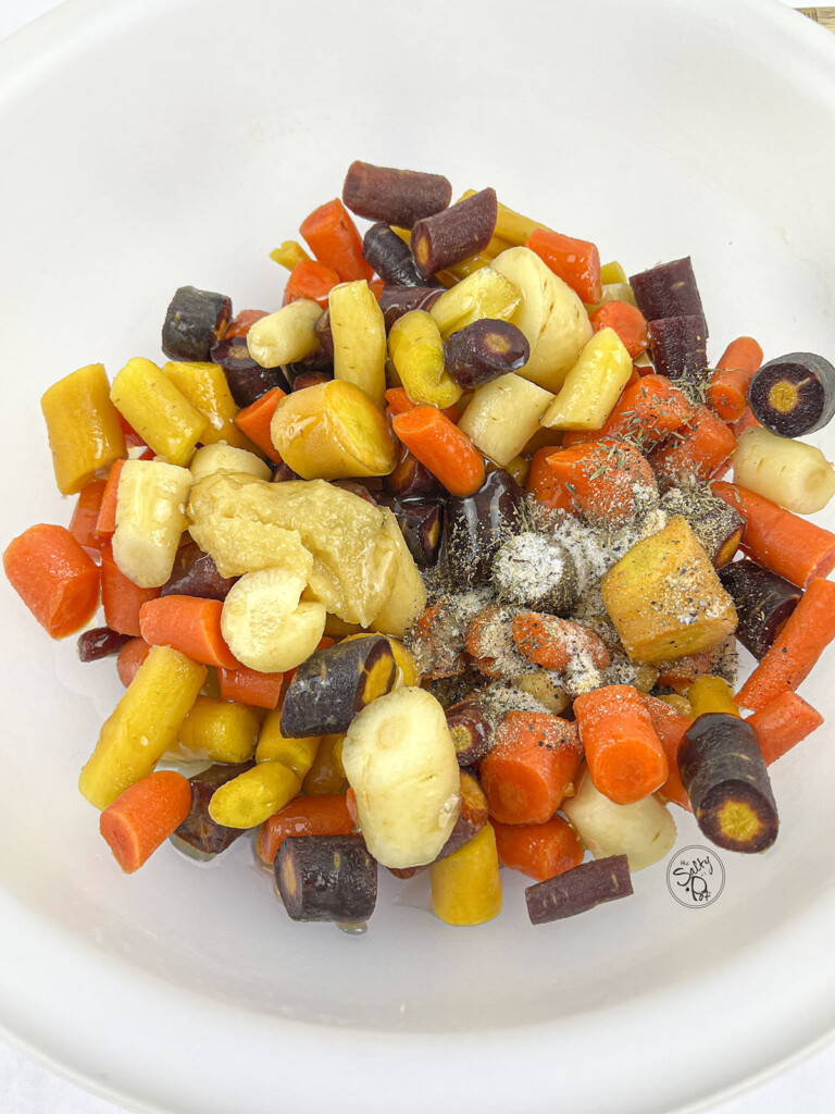 Raw rainbow carrots in a white bowl with seasoning on top.