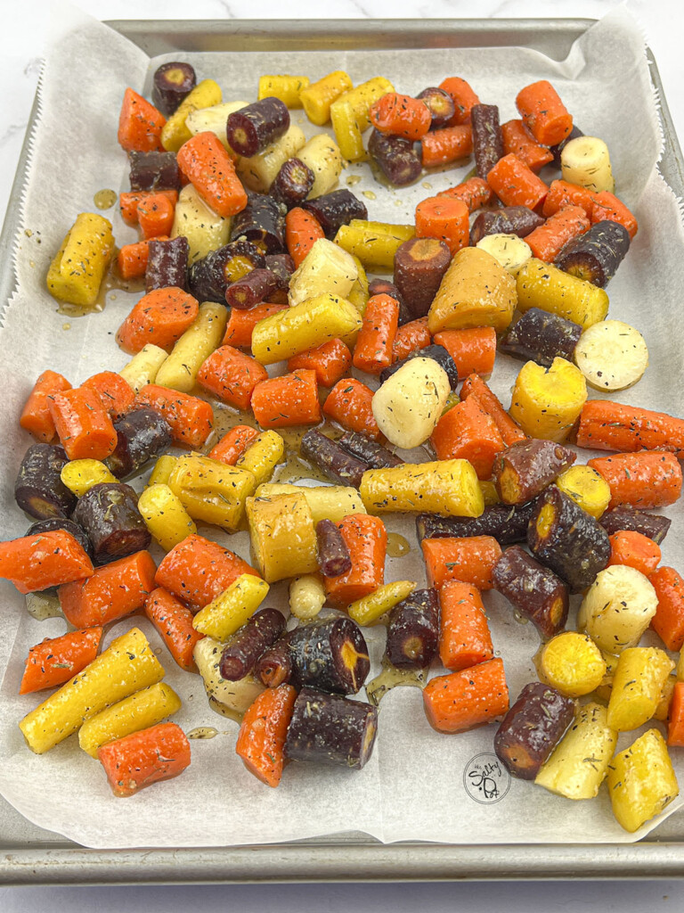 Rainbow carrot pieces on a parchment lined baking dish ready to go in the oven.