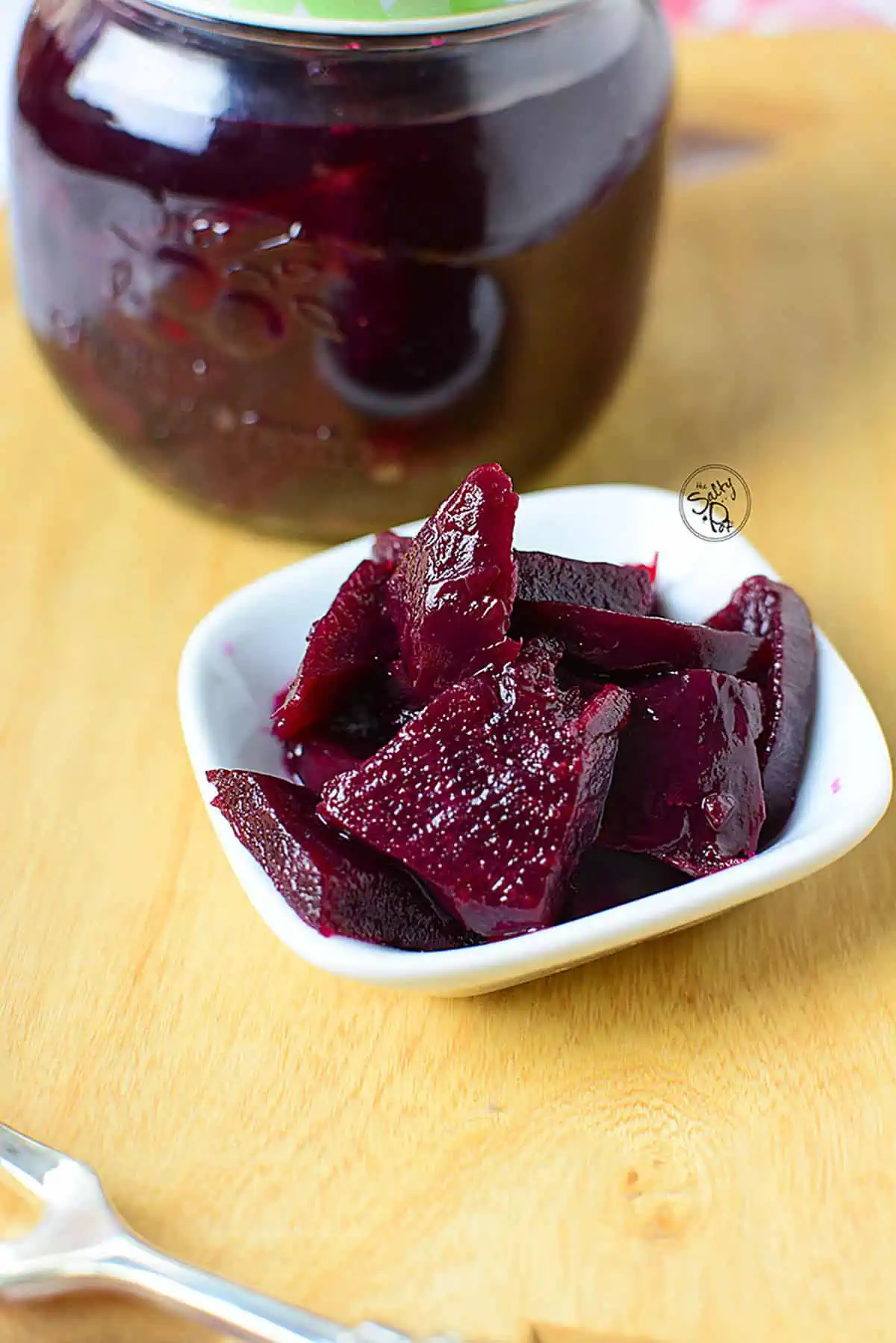 Refrigerator pickled beets in a white serving dish with a jar in the upper left background.
