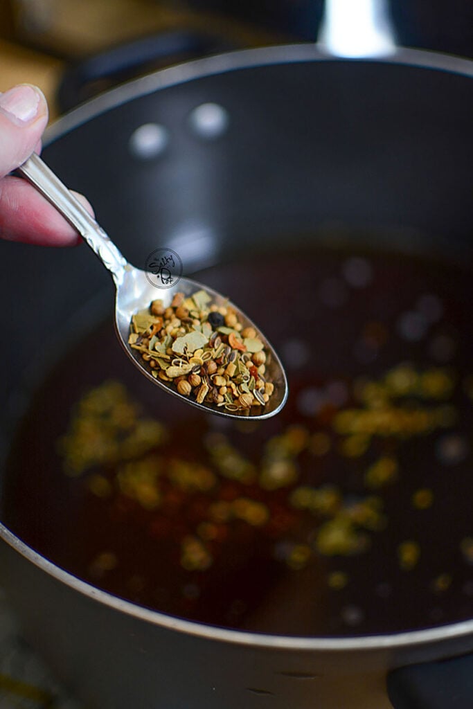 Pickling spice in a spoon over the pot of brine.