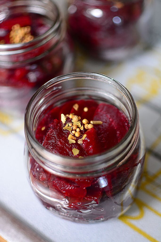 Cooked beets in a jar with a pinch of pickling spice on top.