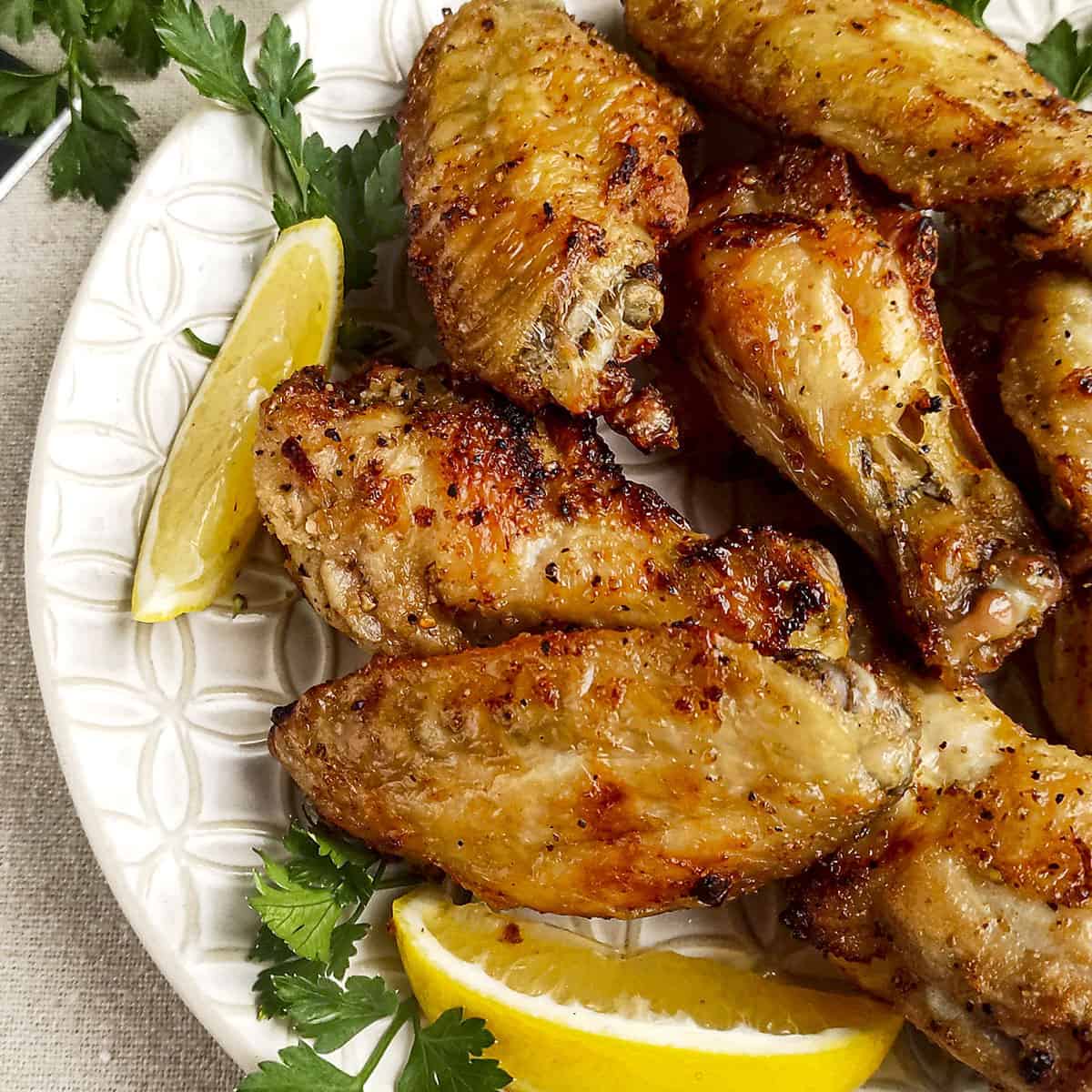 Lemon pepper air fryer chicken wings with a slice of lemon on a white plate square image.