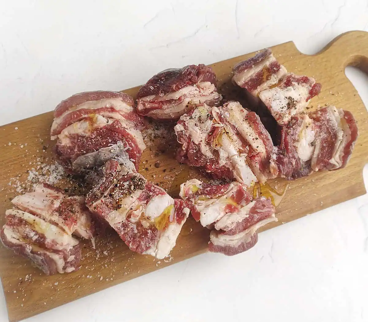Raw beef short ribs seasoned with salt, pepper and olive oil on a wooden cutting board.