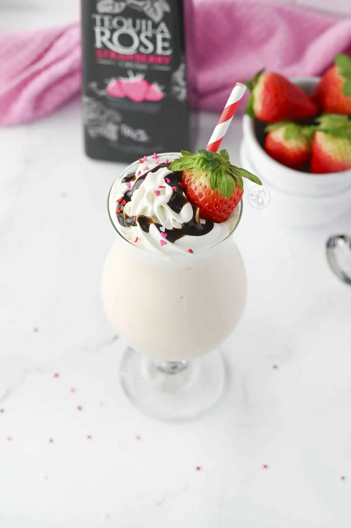 Tequila rose cocktail with a topping of whipped cream, chocolate syrup, and a fresh strawberry, and straw.