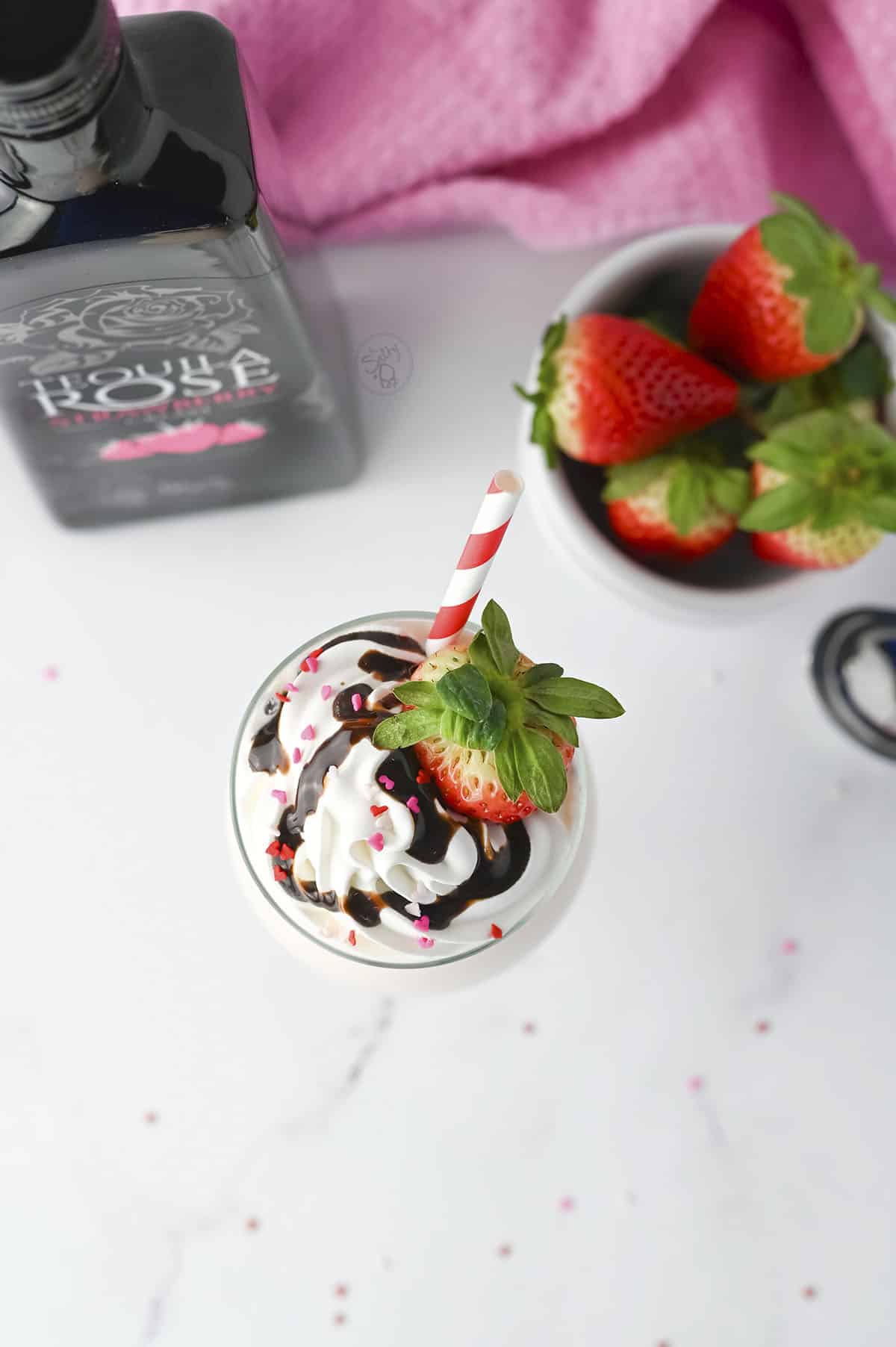 A top down image of the tequila milkshake. The bottle and fresh strawberries are at the top of the photo.