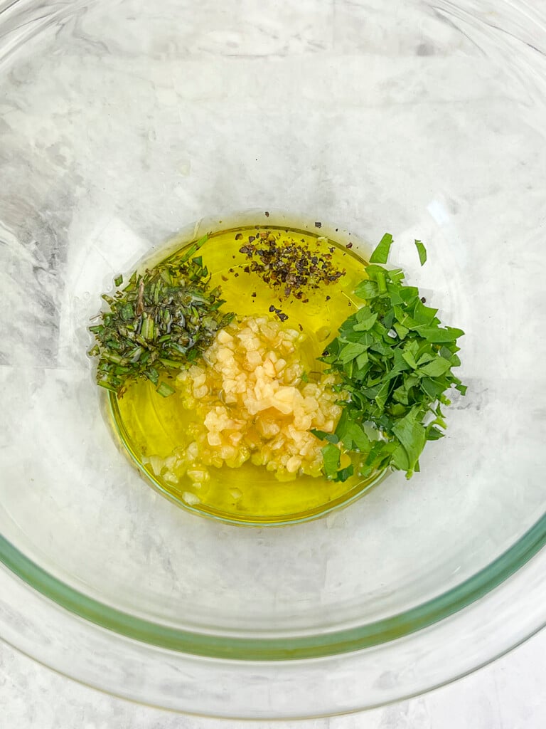In a glass bowl, the oil, garlic and other seasonings are ready to be mixed. 