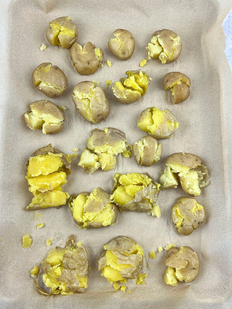 The smashed potatoes are laid out on a parchment lined baking tray. 
