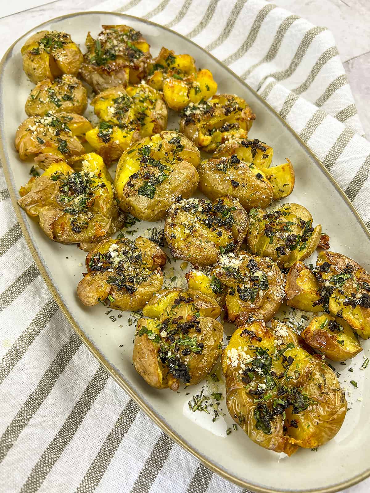 Smashed air fryer new potatoes, garnished in fresh herbs, butter, and parmesan cheese. 
