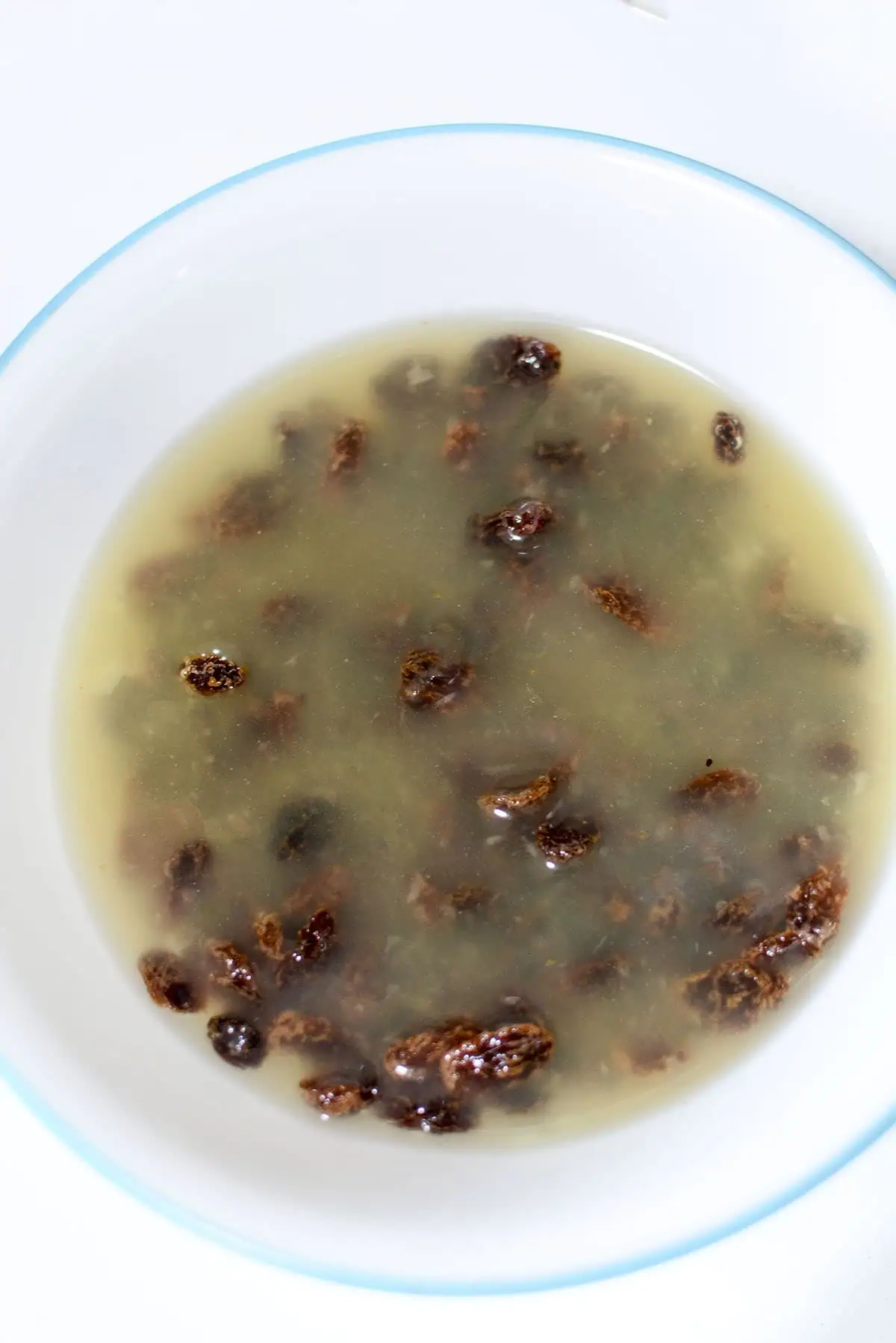 Raisins steeping in pineapple juice in a white bowl. 