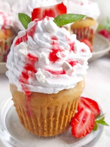 Eton mess cupcake on a glass plate with a strawberry beside it.