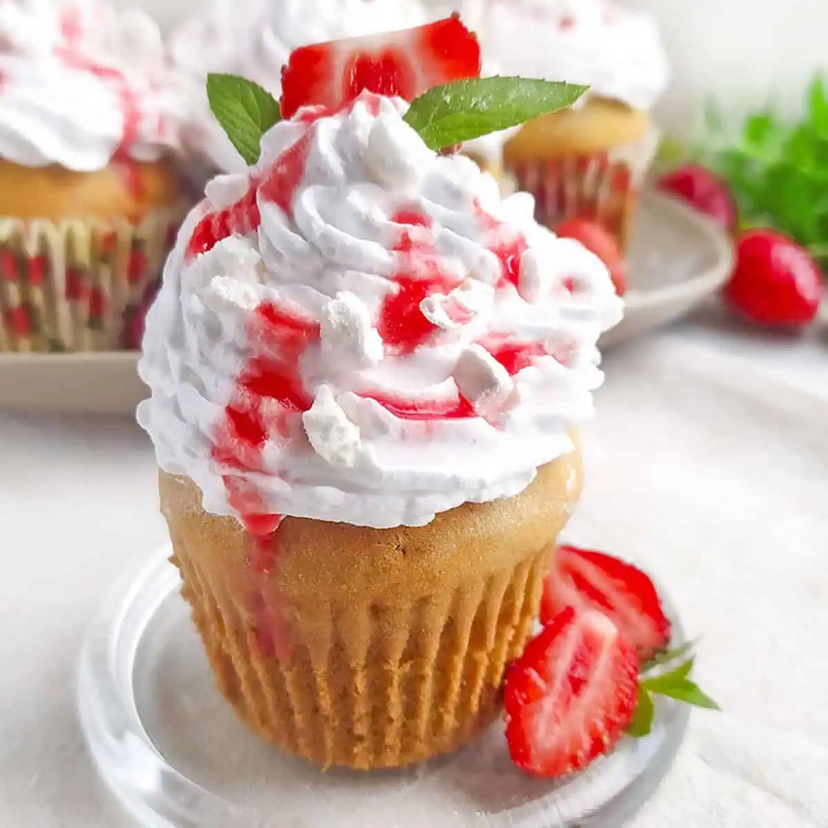 Eton mess cupcake on a glass plate with a strawberry beside it.