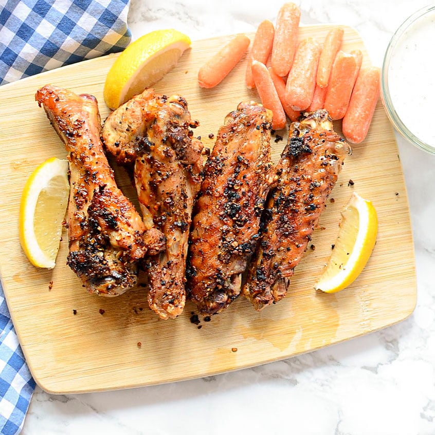 Air fryer turkey wings on a wooden board with carrots and lemon arranged around them.